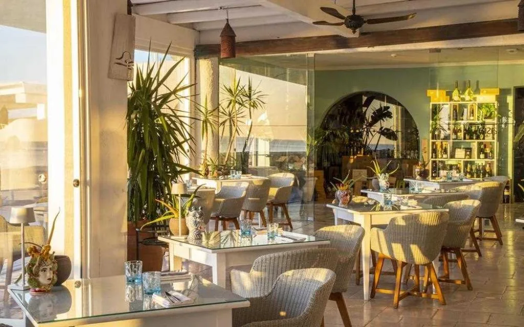 Sala ristorante luminosa con tavoli, poltrone in vimini e piante alla luce del tramonto