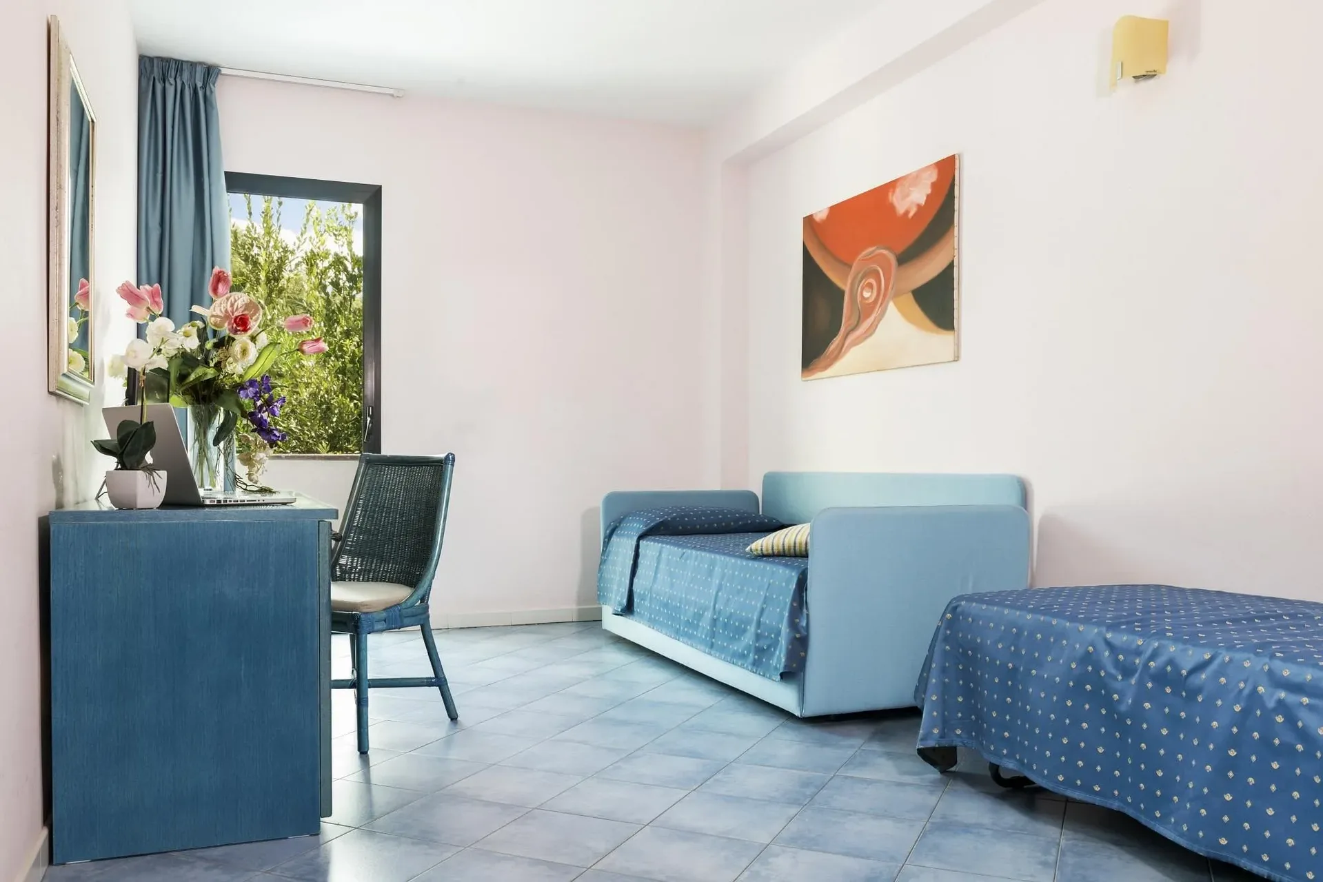 Zona giorno della camera con divano letto blu, scrivania e finestra sul giardino