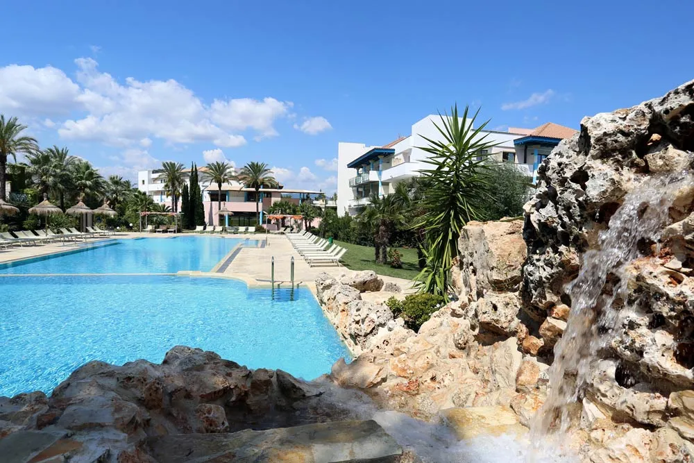 Piscina con cascata artificiale in roccia e vista sugli edifici del resort