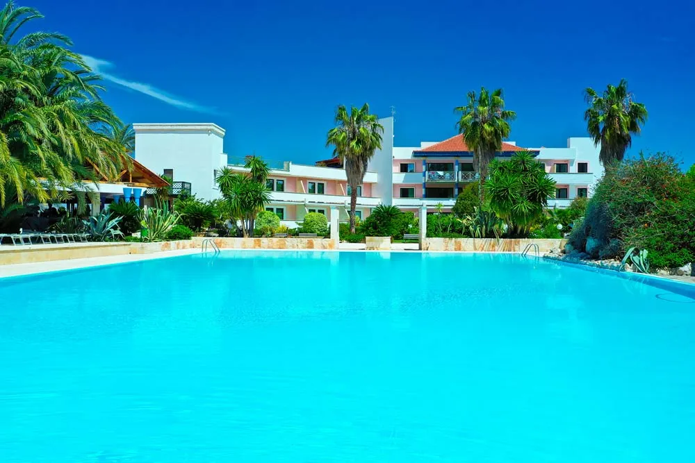 Piscina esterna con acqua azzurra e edificio dell'hotel circondato da palme