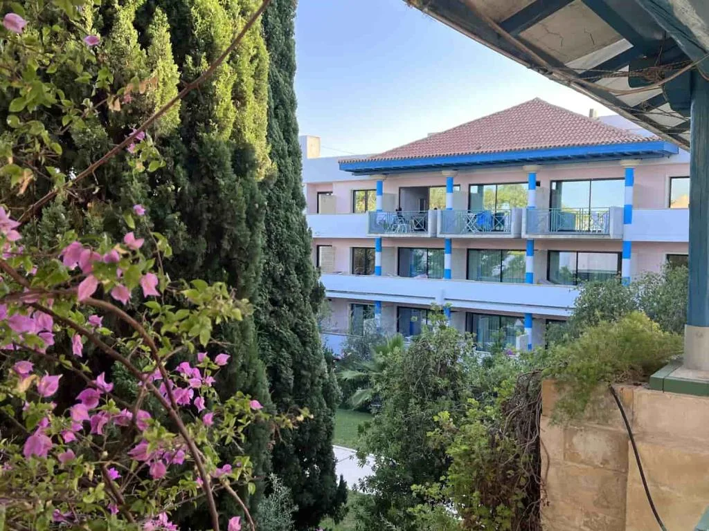 Esterno dell'hotel con balconi, colonne blu e vegetazione con bouganville in fiore