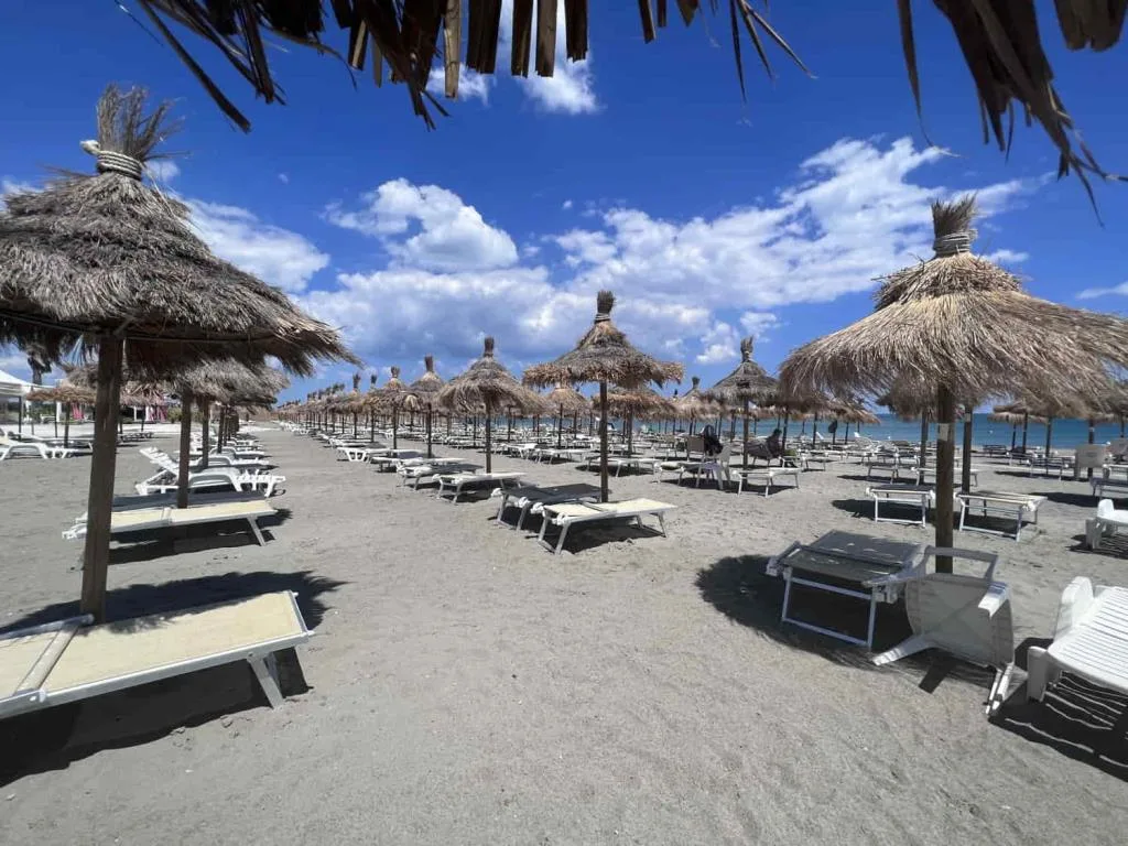 Spiaggia di sabbia con ombrelloni in paglia e lettini vista mare