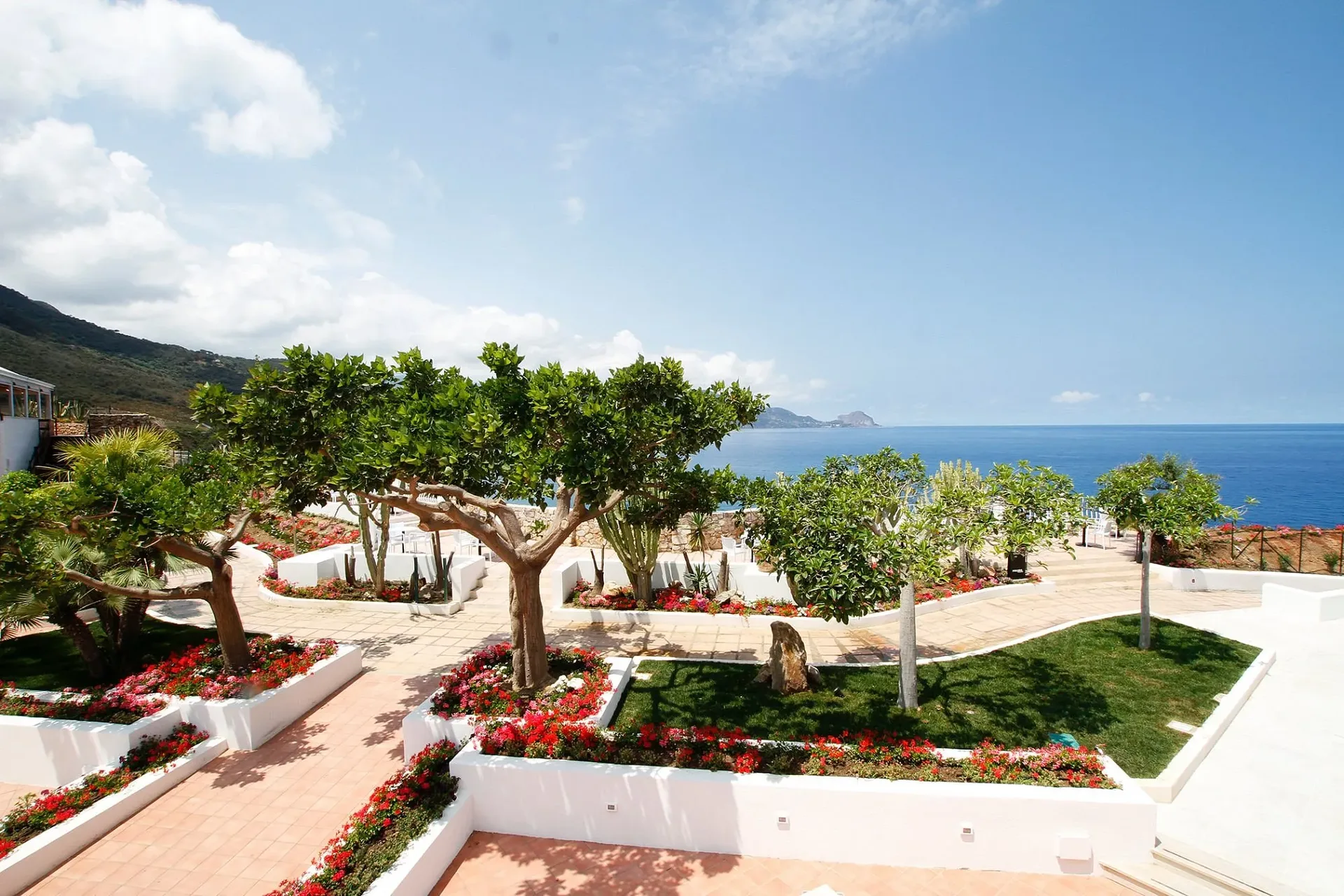 Giardino terrazzato con alberi, fiori rossi e vista panoramica sul mare