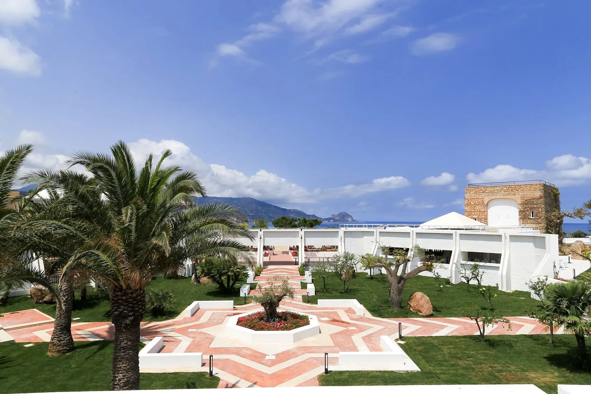 Giardino con palme, aiuola centrale a stella e antica torre in pietra vista mare