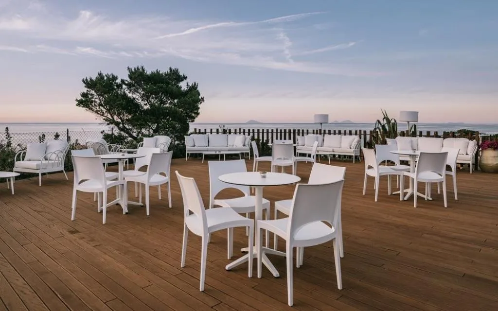 Terrazza esterna con tavoli e sedie bianche affacciata sul mare al tramonto