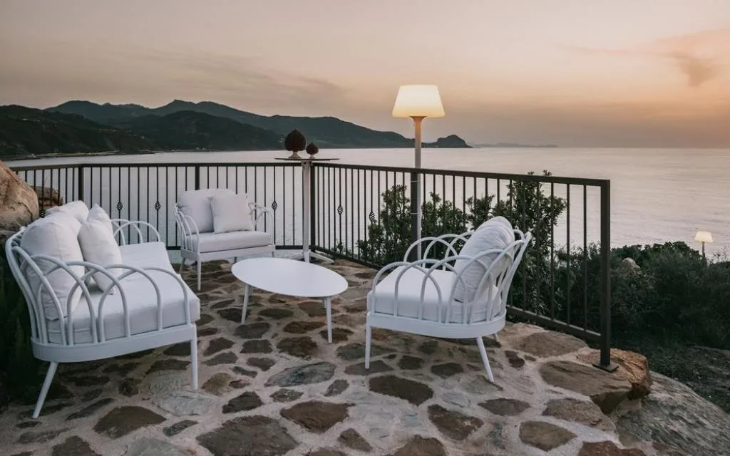 Terrazza panoramica con poltroncine bianche e vista sulla costa al tramonto