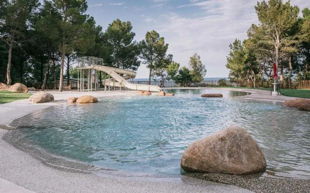 Piscina per bambini con scivolo immersa nel verde e tra i pini
