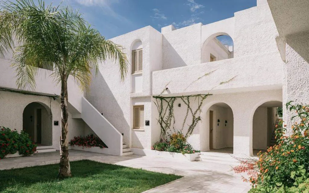 Edificio bianco in stile mediterraneo con palma, archi e giardino fiorito