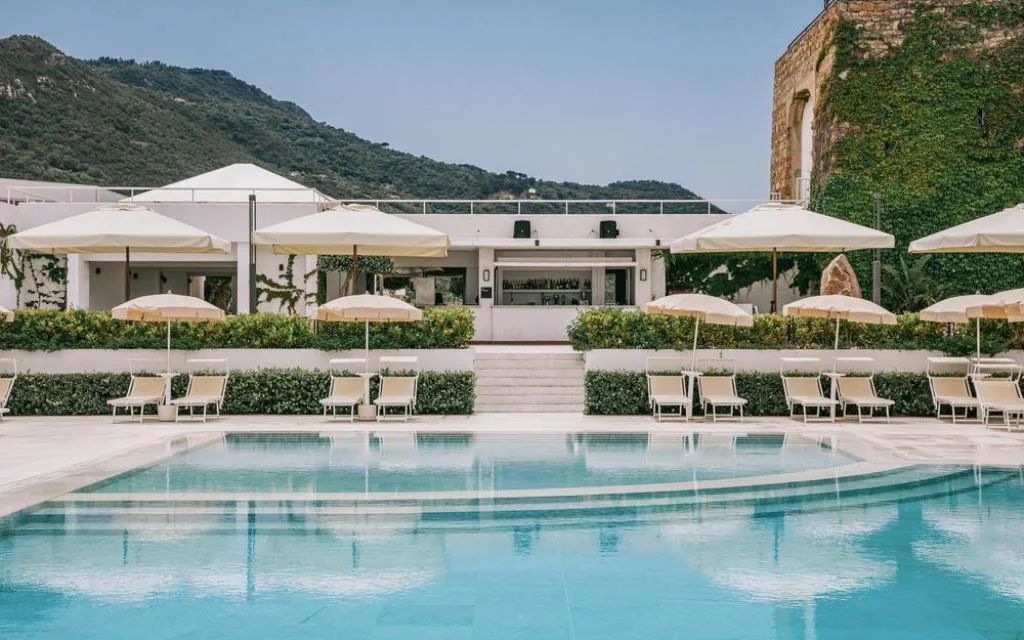 Piscina esterna con lettini, ombrelloni e bar sullo sfondo delle montagne