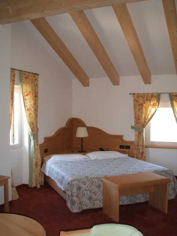 Camera mansardata con testiera in legno chiaro e tende floreali