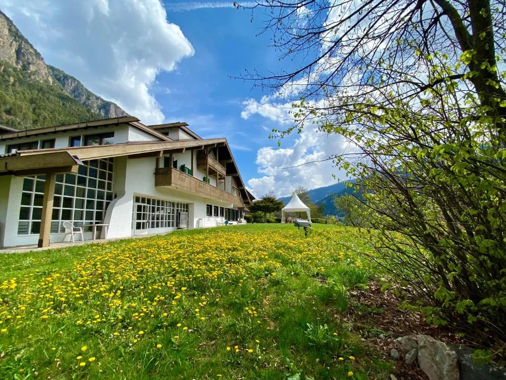 Esterno dell'hotel con prato fiorito, gazebo e montagne sullo sfondo in primavera