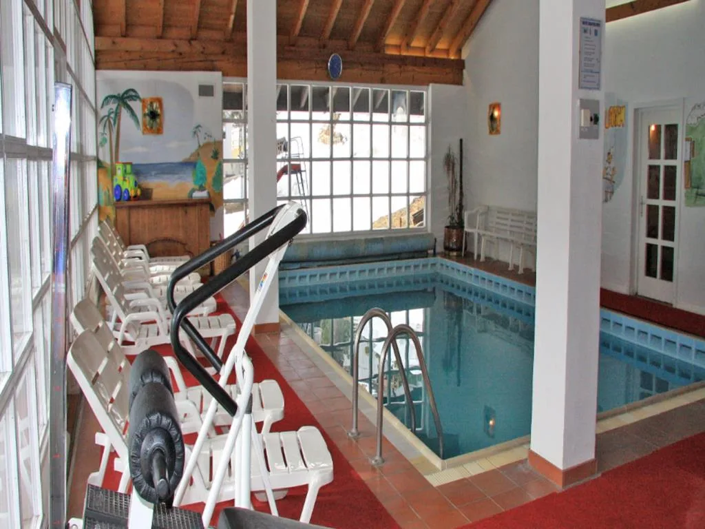 Piscina interna con lettini bianchi e attrezzatura fitness accanto alle vetrate