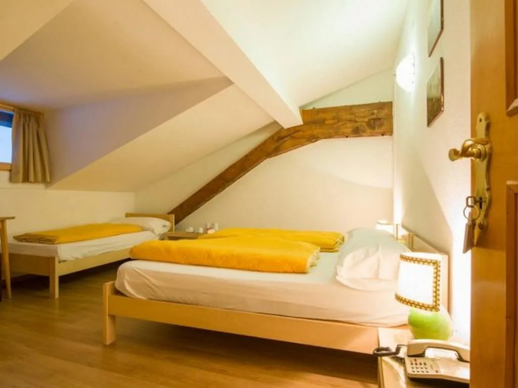 Camera mansardata con letti singoli, coperte gialle e travi in legno a vista