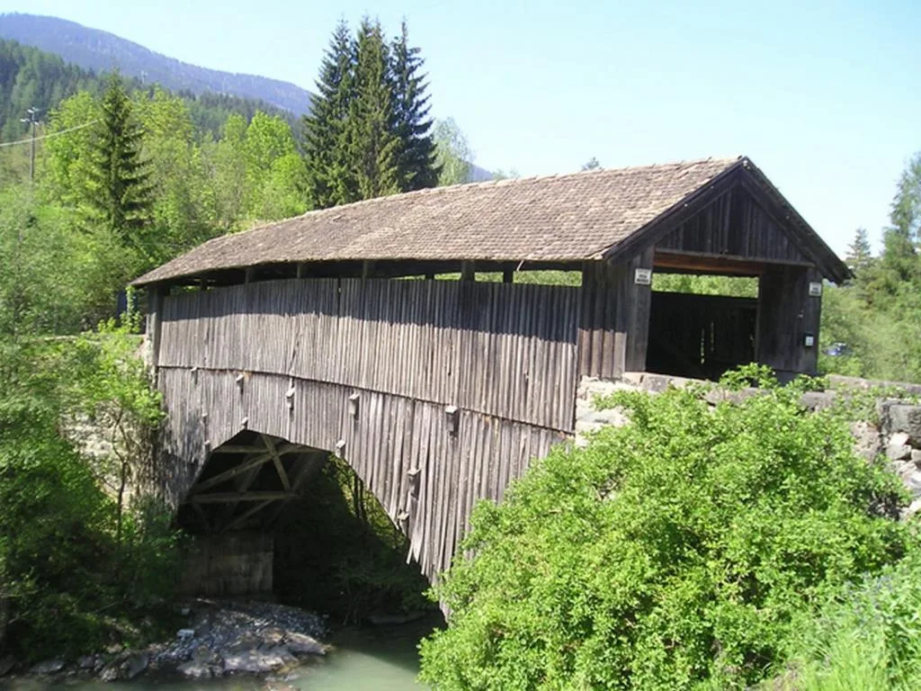 Antico ponte coperto in legno sopra un torrente circondato dal verde
