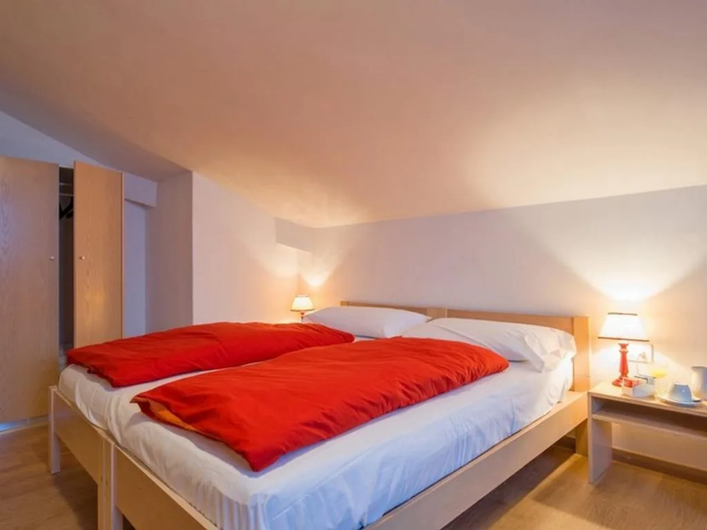Camera con letto matrimoniale, piumini rossi e comodino con lampada