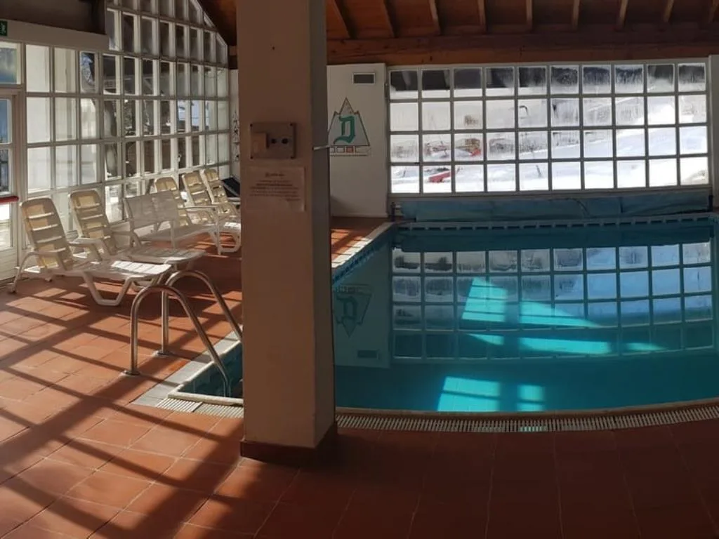Piscina interna con lettini bianchi e mattonelle di vetro illuminate dal sole