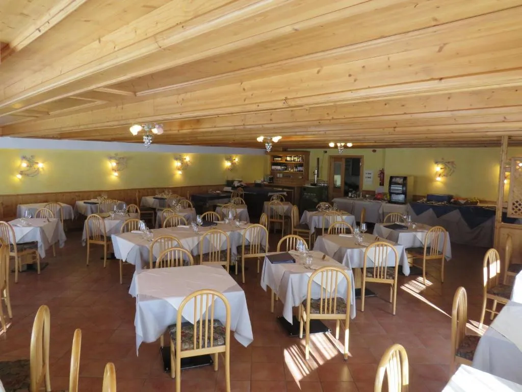 Sala da pranzo luminosa con soffitto in legno, tavoli e sedie in stile alpino