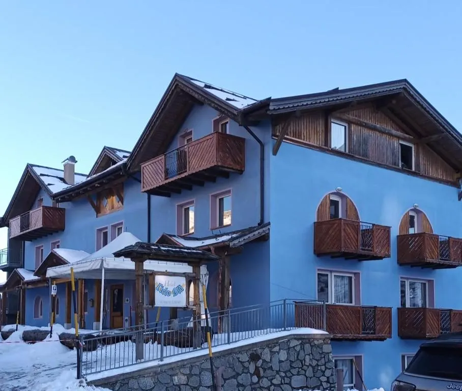 Facciata azzurra dell'hotel con balconi in legno e neve al tramonto invernale