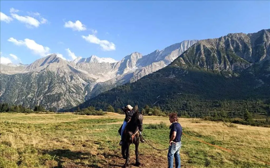 Persona a cavallo con guida in un prato di montagna circondato dalle Alpi
