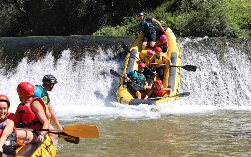 Gruppo di persone durante un'esperienza di rafting su un fiume con cascata