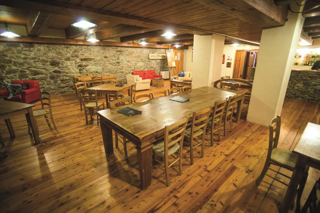 Sala da pranzo rustica con pareti in pietra, grandi tavoli in legno e soffitto a travi
