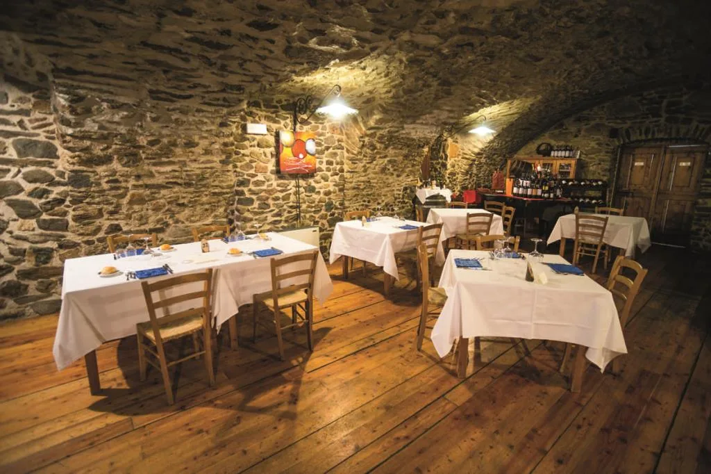 Sala ristorante rustica con volte in pietra, tavoli apparecchiati con tovaglie bianche e pavimento in legno