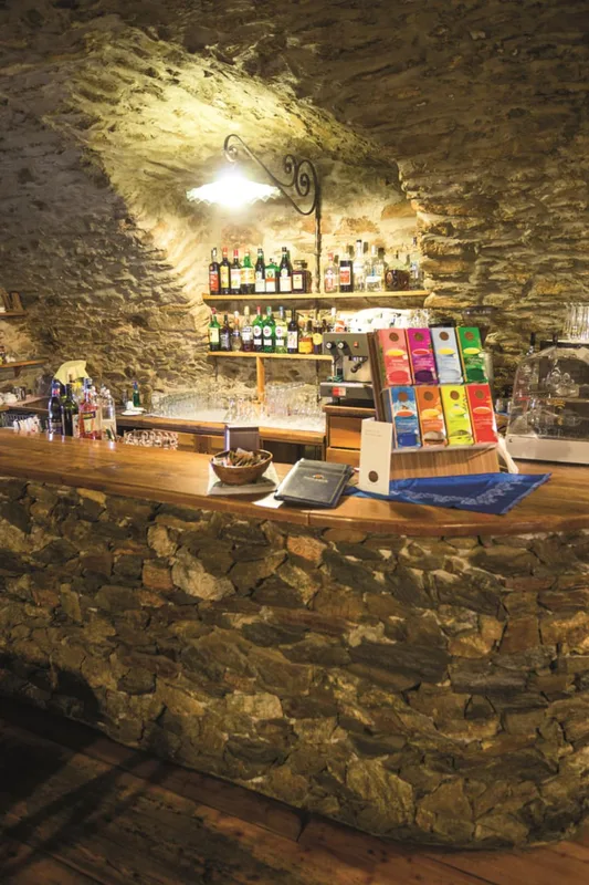 Bar rustico con bancone in pietra e legno, bottiglie di liquori e macchina del caffè sotto una volta in pietra