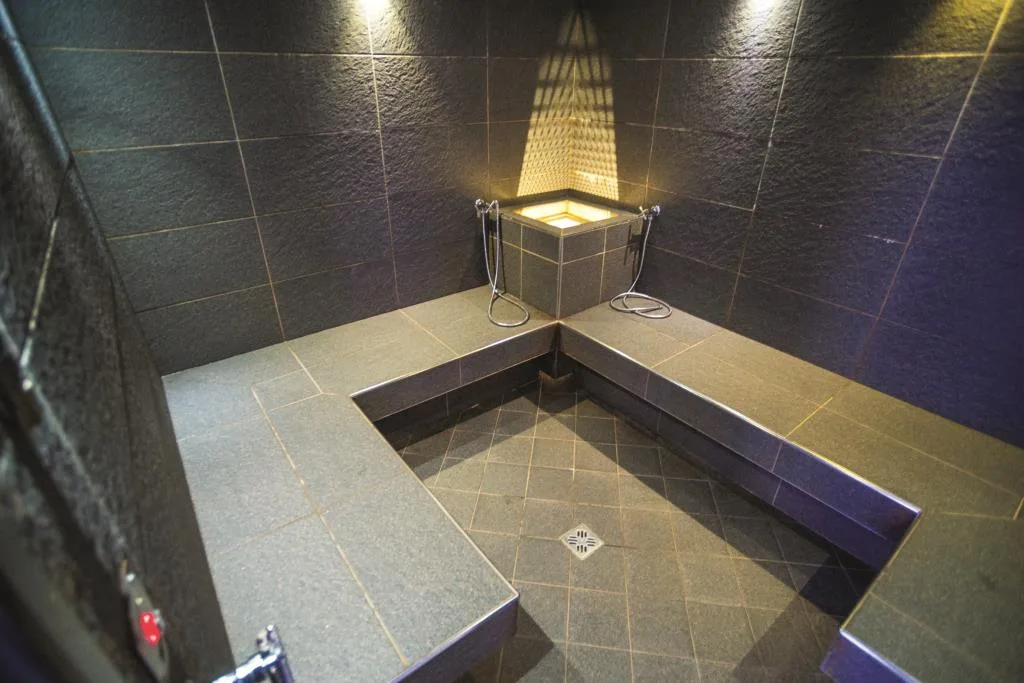 Bagno turco moderno con rivestimento in pietra scura, panche angolari e illuminazione soffusa
