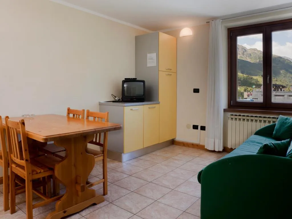 Soggiorno con tavolo in legno, TV, mobili gialli e divano verde con vista sulle montagne
