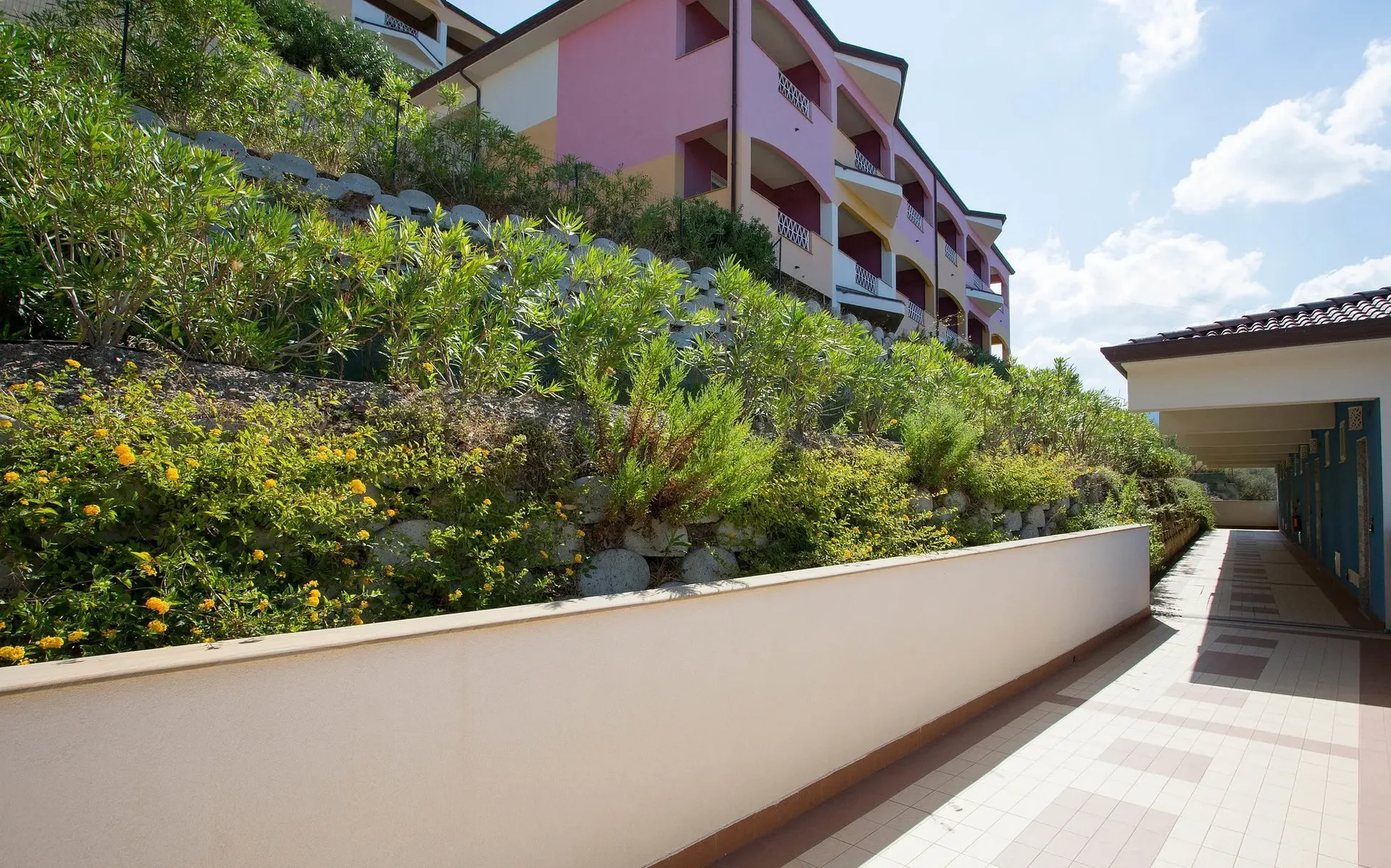Vialetto esterno dell'hotel con edifici colorati e giardino fiorito in collina