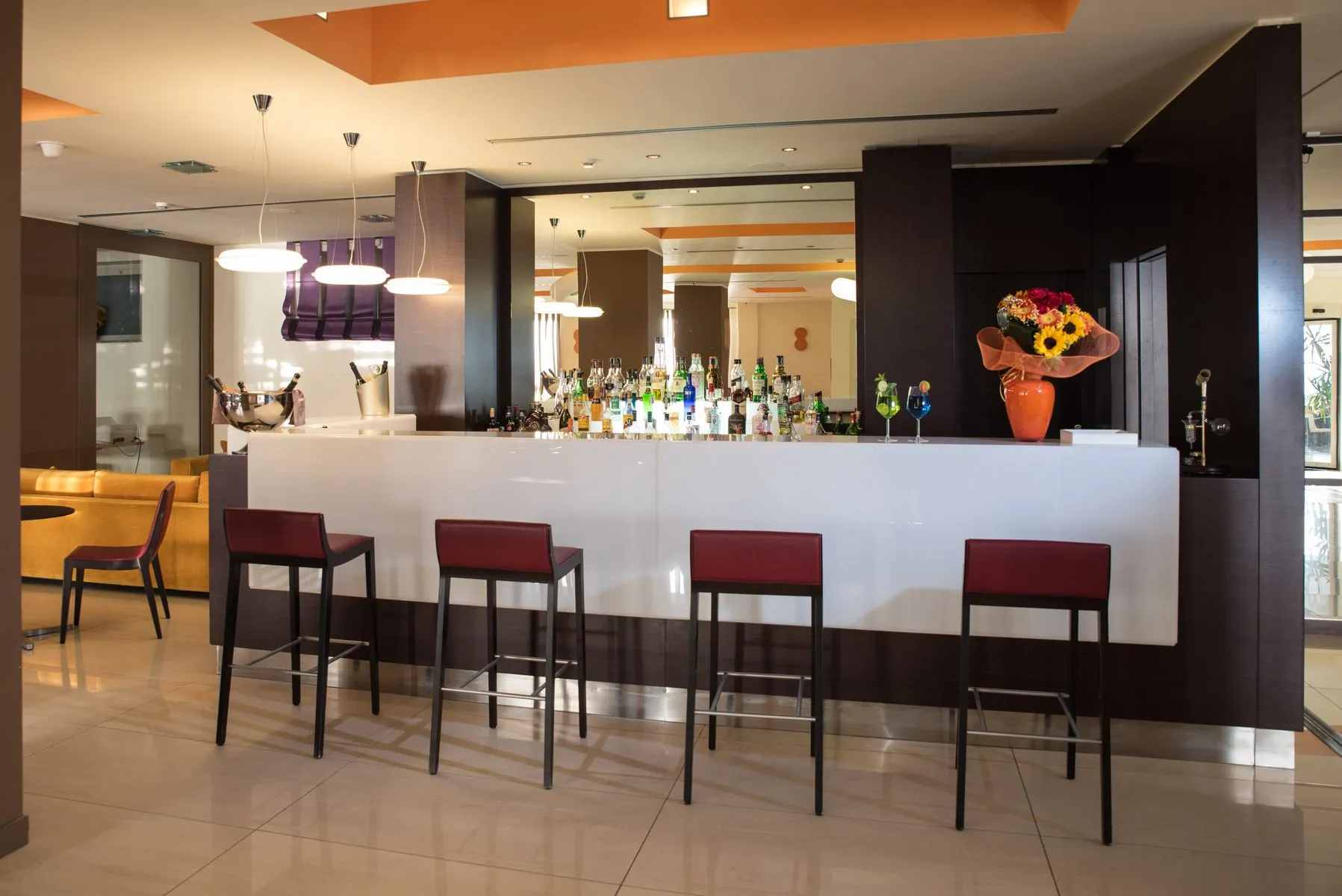 Bar dell'hotel con bancone bianco, sgabelli rossi e bottiglie