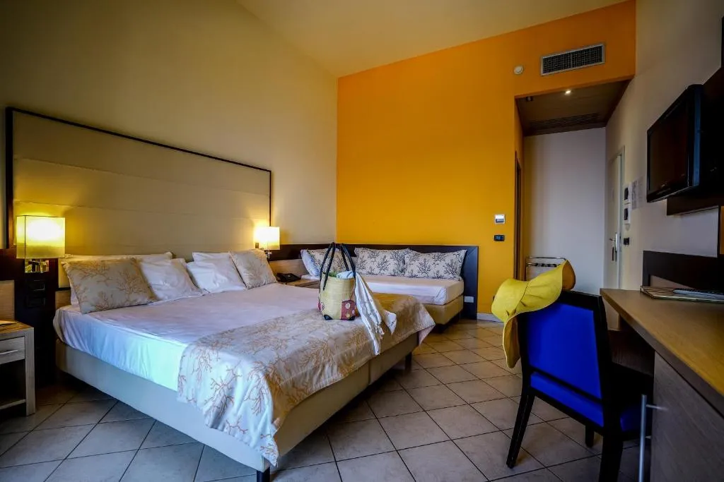Camera tripla con letto matrimoniale e divano, parete arancione e scrivania
