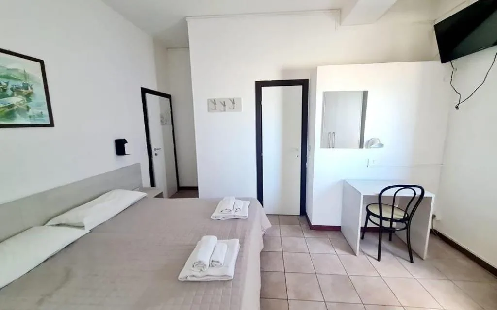 Camera matrimoniale bianca con scrivania, sedia e TV a parete
