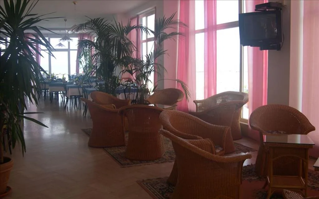Sala interna con poltrone in vimini, piante e ampie vetrate con tende rosa