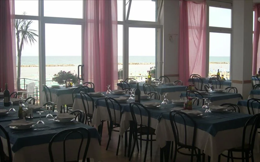 Sala ristorante con tavoli apparecchiati e vista mare dalle grandi vetrate