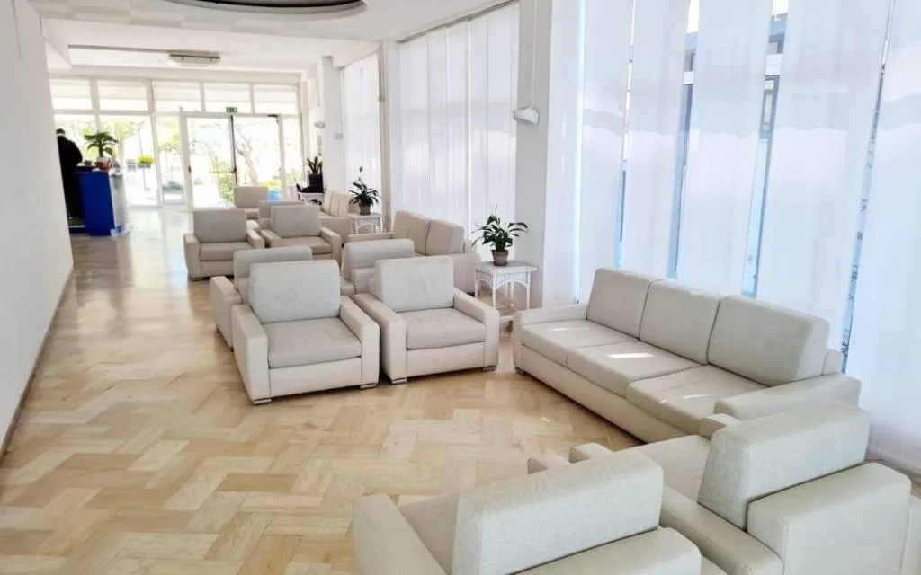 Ampia hall con divani e poltrone chiare su pavimento in parquet
