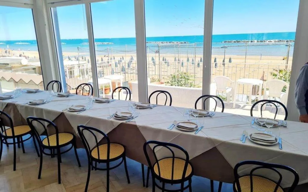 Sala ristorante con tavoli apparecchiati e vista panoramica sulla spiaggia