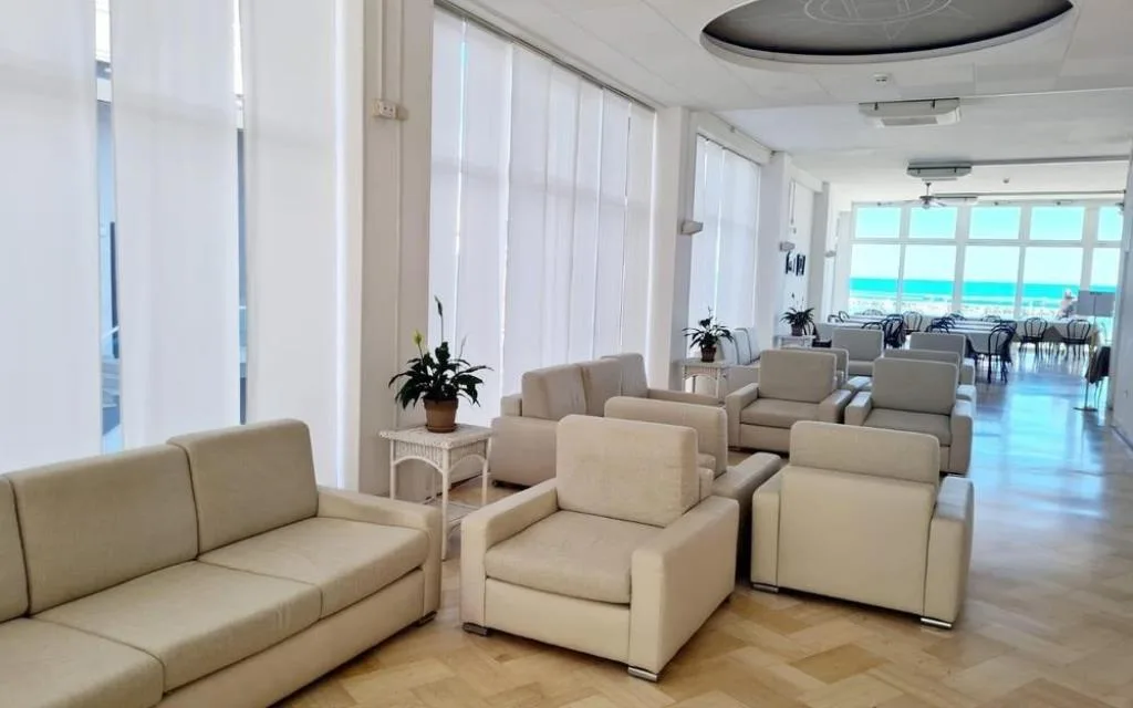 Sala comune con poltrone chiare e ampie vetrate con vista mare