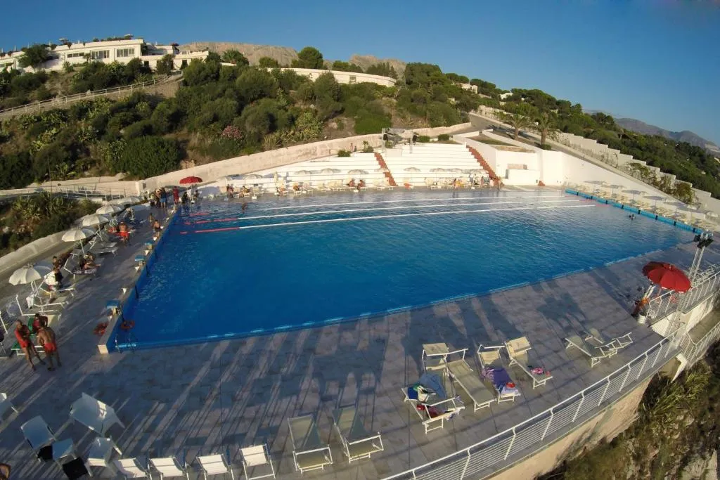 Ampia piscina con lettini e ombrelloni circondata dalla collina