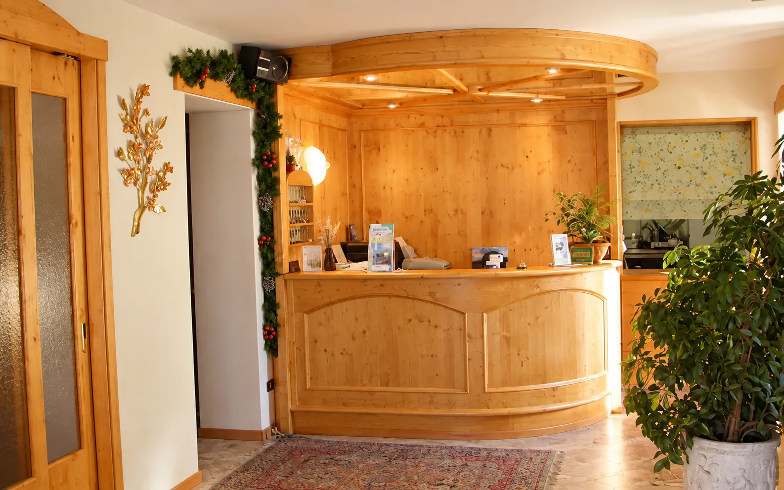 Reception dell'hotel con banco in legno chiaro, decorazioni natalizie e pianta verde