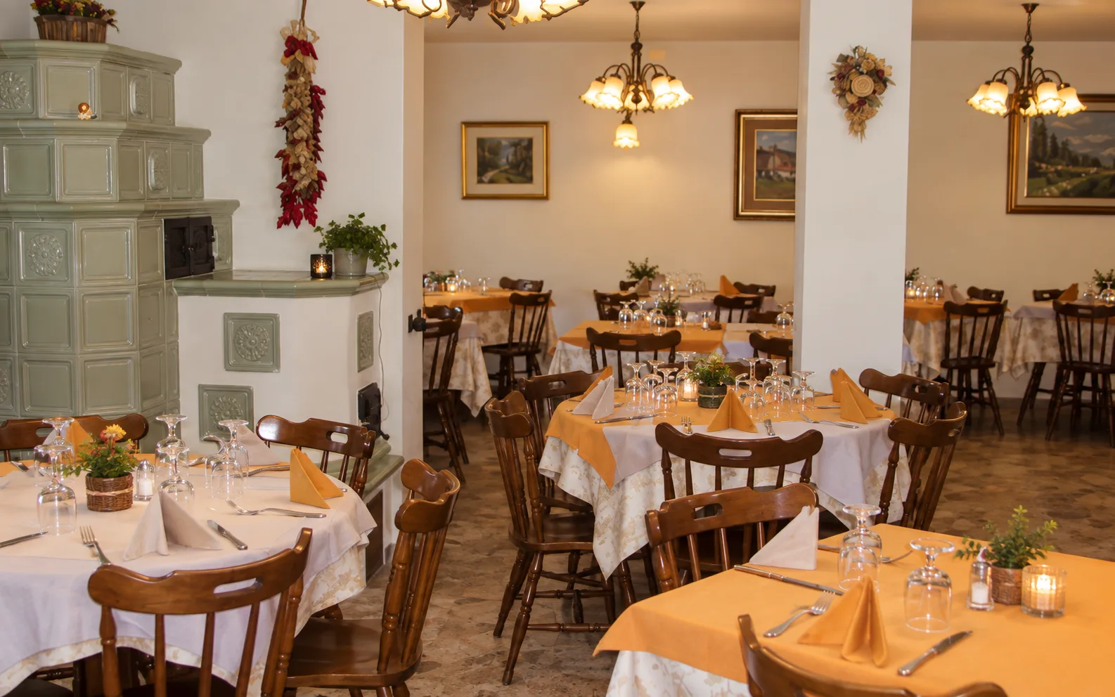 Sala ristorante con tavoli apparecchiati, tovaglie arancioni e tradizionale stufa in maiolica