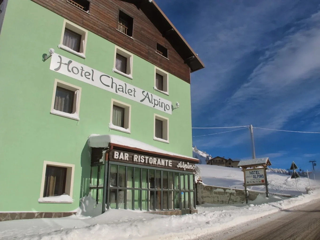 Dettaglio della facciata dell'Hotel Chalet Alpino con insegna e bar ristorante sotto la neve
