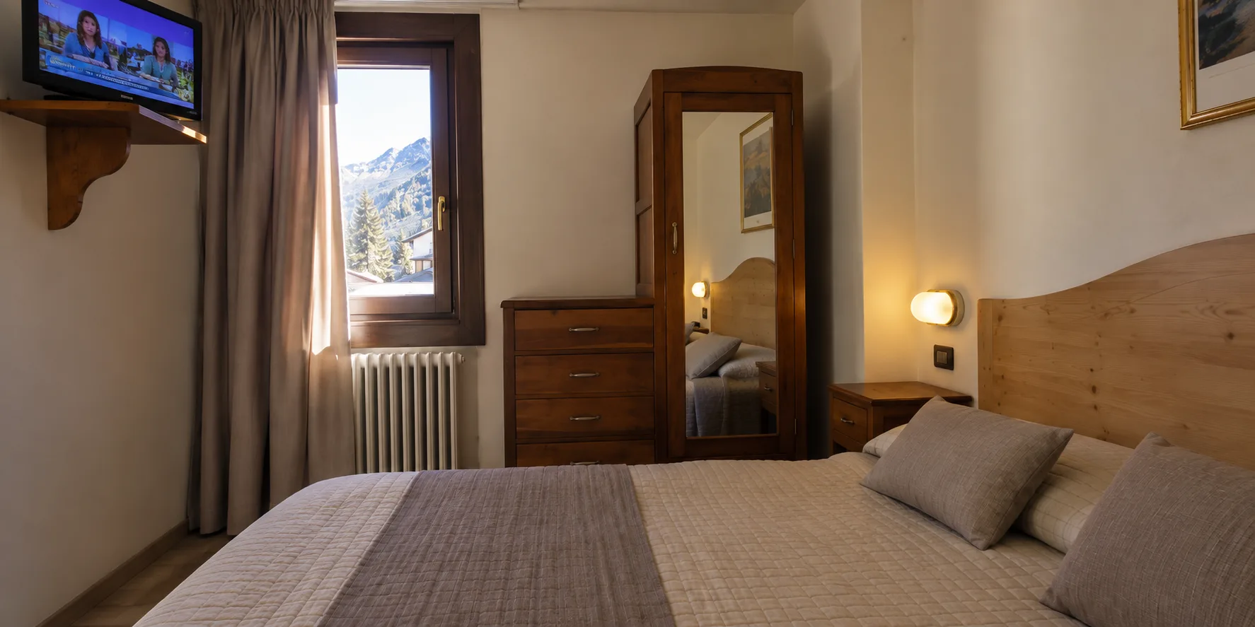Camera da letto con letto matrimoniale, TV, cassettiera in legno e vista sulle montagne