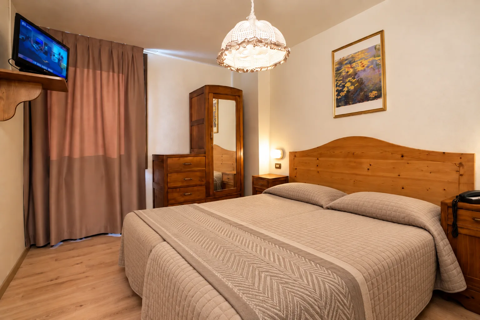 Camera matrimoniale con arredi in legno, TV a parete e lampadario decorativo