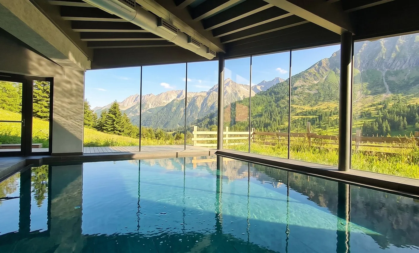 Piscina interna con vetrate e vista estiva su montagne e prati verdi