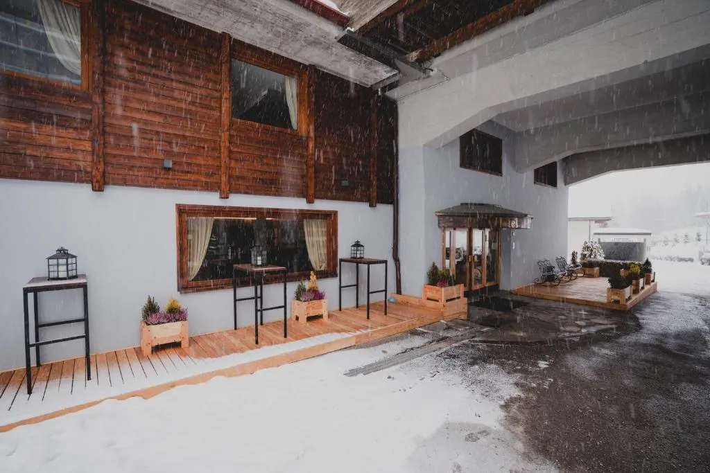 Ingresso dell'hotel con veranda in legno e tavoli alti durante una nevicata