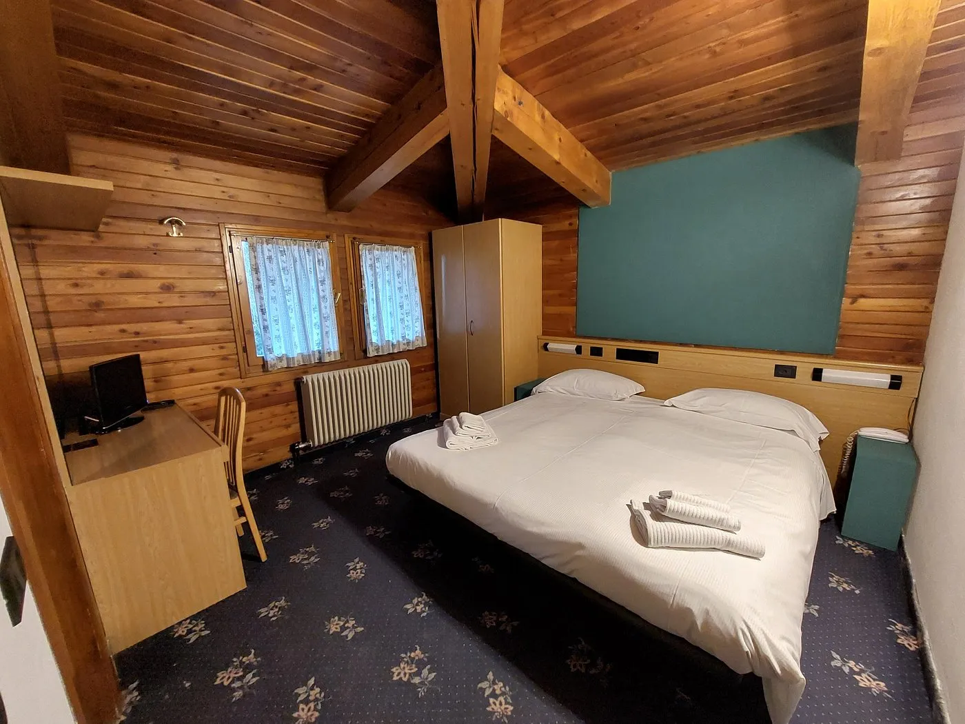 Camera matrimoniale con soffitto e pareti in legno, scrivania e parete verde