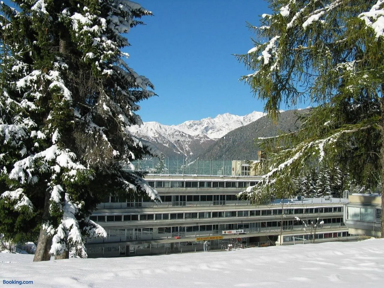 Struttura innevata tra abeti carichi di neve con montagne sullo sfondo