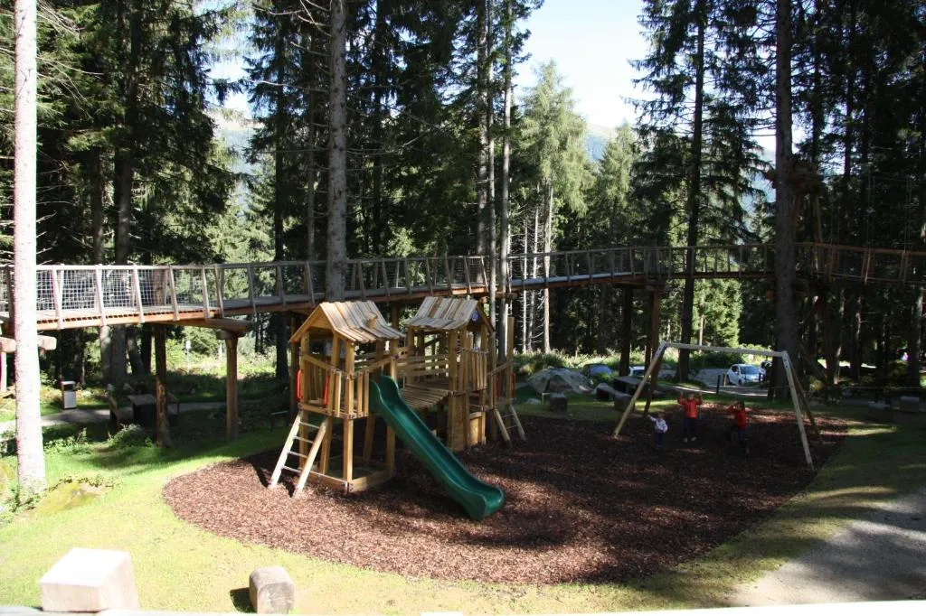 Parco giochi per bambini nel bosco con scivolo, altalene e passerella sospesa