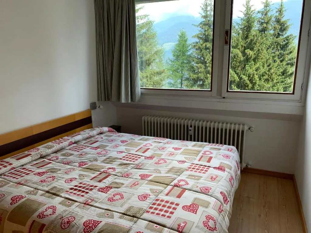 Camera matrimoniale con copriletto decorato e finestra con vista sugli abeti